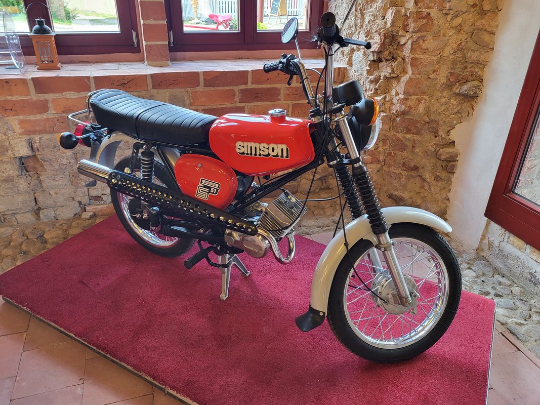 Auf dem Foto zu sehen ist ein Moped der Marke Simson in der Ausführung S51 Enduro. Sie steht auf einem roten Teppich auf ihrem Hauptständer, der Lenker leicht nach links geneigt. Das Foto wurde im Brauhaus Himmelpfort aufgenommen.